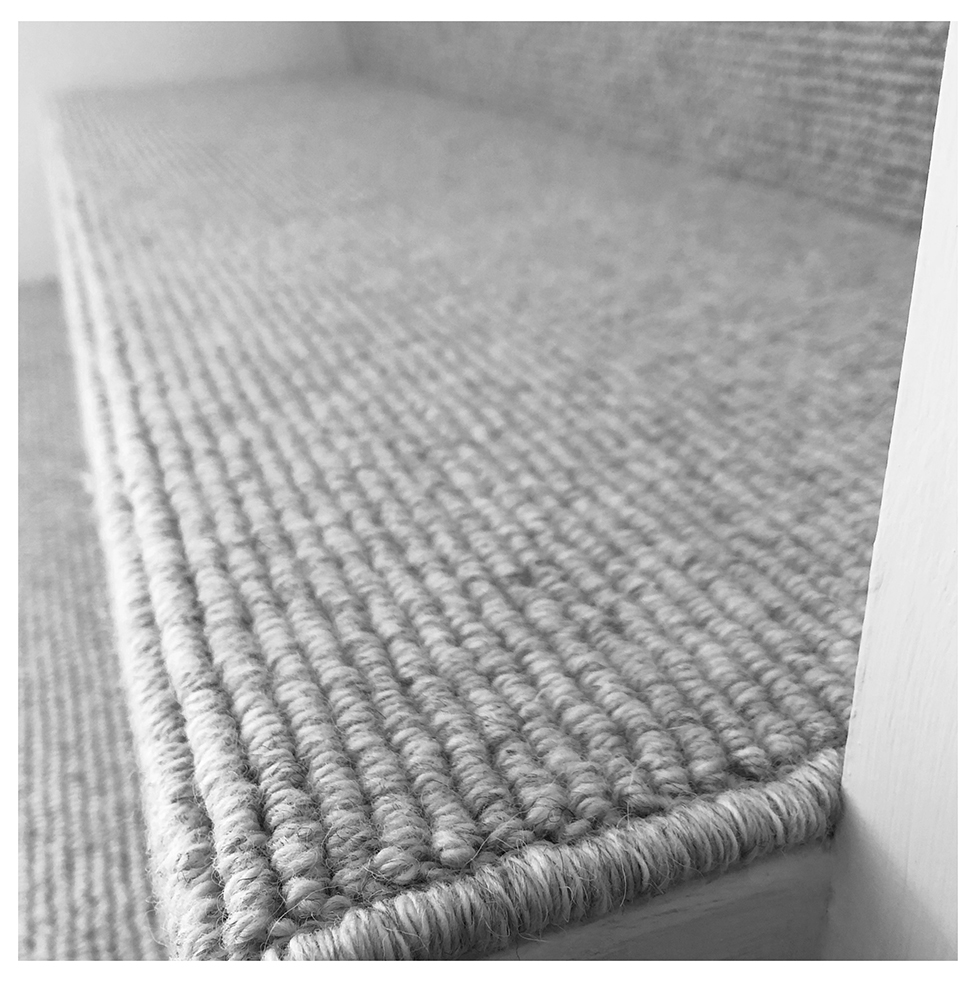 Close-up of a textured woven carpet runner along a hallway, with a white baseboard visible on the right.