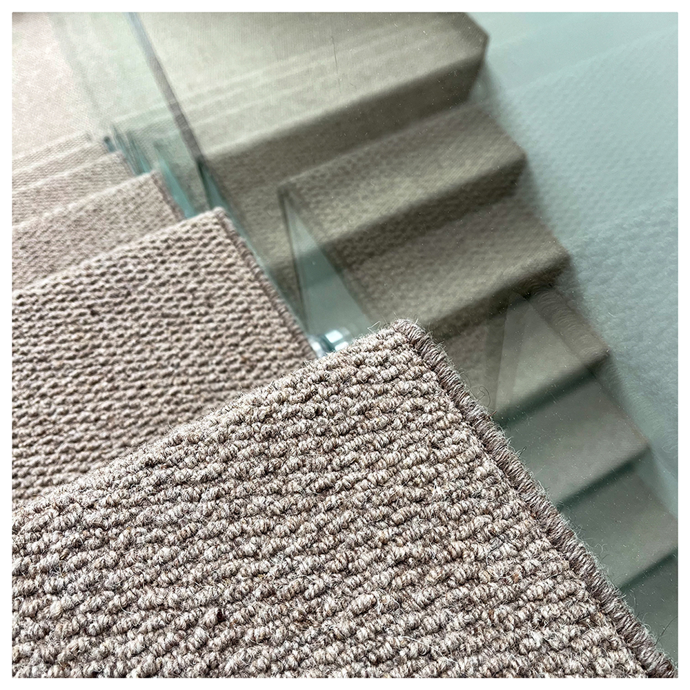 Close-up of brown textured carpet on a staircase with a glass railing in the background.